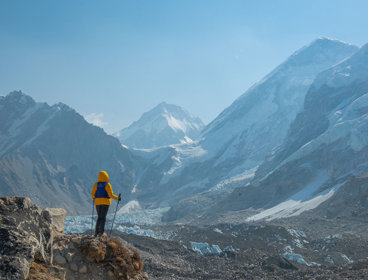 A backpacker wearing a bright yellow coat taking in the view on a mountain walk in the Himalayas.