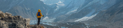 A backpacker wearing a bright yellow coat taking in the view on a mountain walk in the Himalayas.