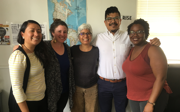 A group of five people smiling for picture in front of map on the wall. Laura Pulido stands in the middle.