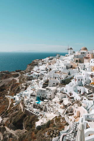 White buidldings covering a hillside with bright sunlight and sea in the background