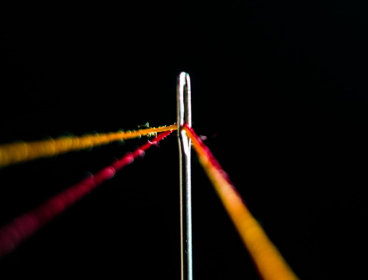 Strings of yellow and red thread in needle against black background.