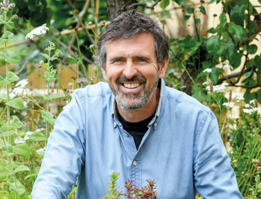 Person in a garden standing amongst green plants.