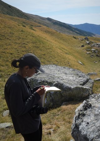 Researcher stood on a mountain slope writing in a notebook. 