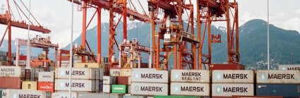 Shipping containers on a boat, with red cranes at the side ready to lift them on and off. 