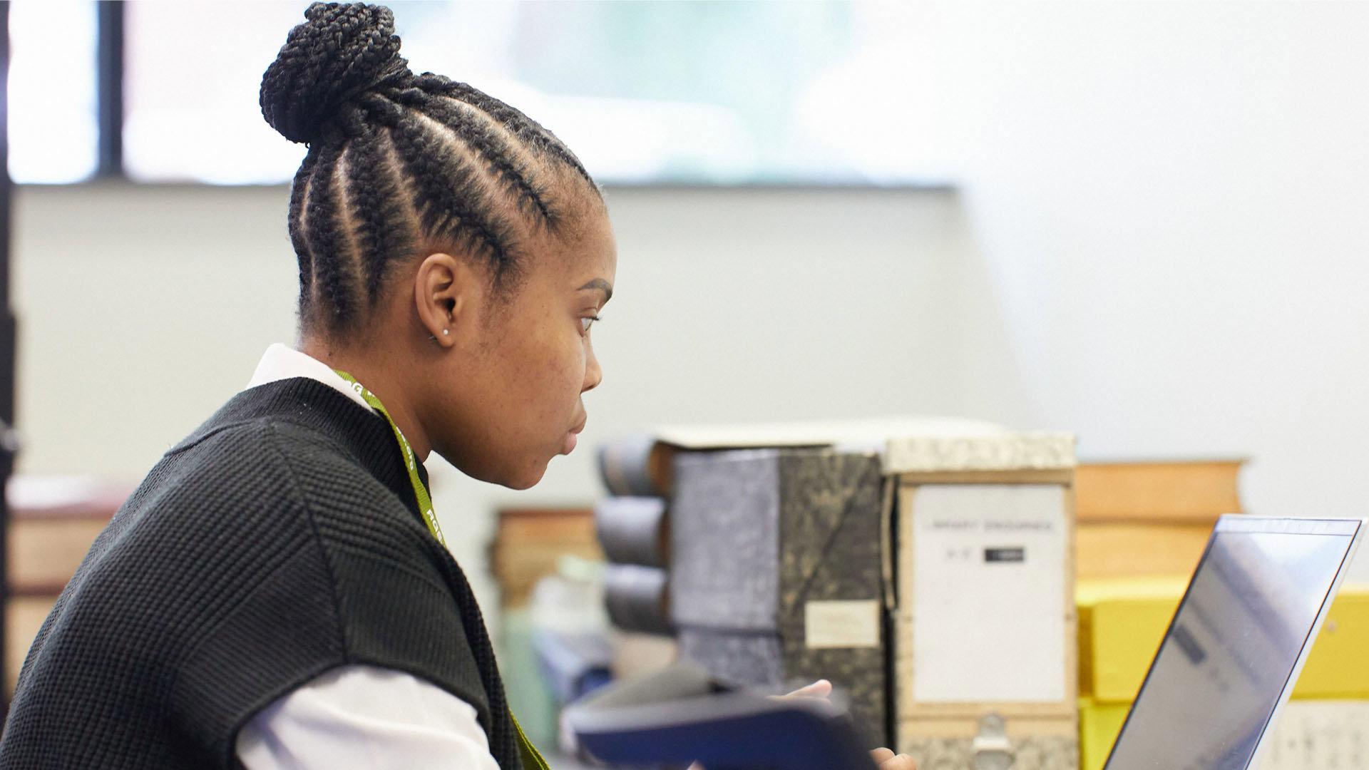 A young person sits at a desk looking at their laptop.