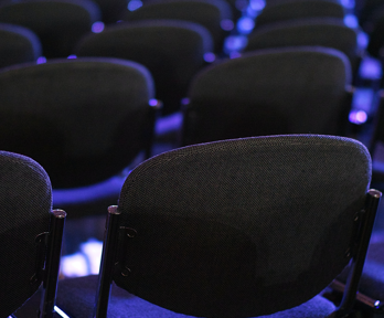 Rows of black chairs which glow slightly blue because of the lighting stretch back beyond view.