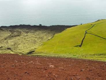 Aerial photo showing the contrast between volcanic stones and green grass right next to the sea.