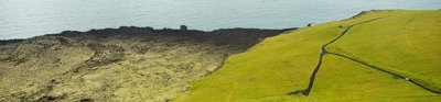 Aerial photo showing the contrast between volcanic stones and green grass right next to the sea.