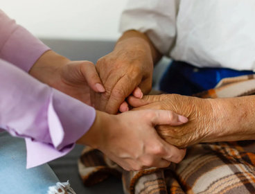 Close up of two people, including one elderly person, holding hands in a reassuring manner.