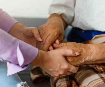 Close up of two people, including one elderly person, holding hands in a reassuring manner.