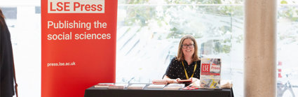 LSE Press stall at the RGS-IBG Conference with a person sitting behind the booth. A red banner reads 'LSE Press: Publishing the social sciences'.