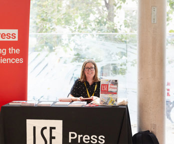 LSE Press stall at the RGS-IBG Conference with a person sitting behind the booth. A red banner reads 'LSE Press: Publishing the social sciences'.