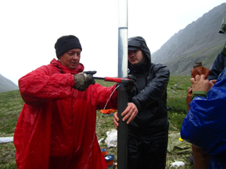 Two people stood in the rain draining water from a core on a mountainside.