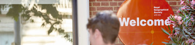 People walk into the RGS at Exhibition Road. An orange welcome sign is focused in on.