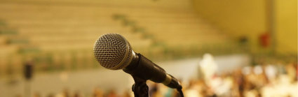 Close-up of a microphone on stand in front of a blurred out crowd of people.