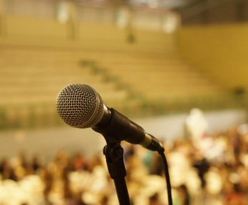 Close-up of a microphone on stand in front of a blurred out crowd of people.