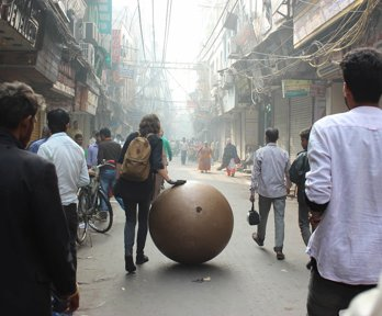 Streetscene with people and large bronze ball sculpture being wheeled along the street
