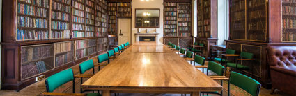 A large wooden table setup for a boardroom meeting in the Lowther Room at the Society. The table is surrounded by large bookcases full of books.