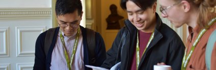 Three people looking at a conference programme and holding coffee cups