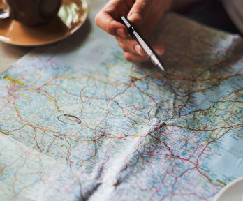 Close up of a hand holding a pan and a map spread out on a table.