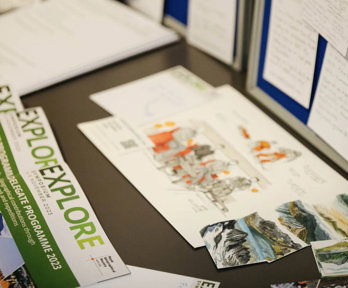 Tabletop full of images of mountains and leaflets from the Society's Explore symposium 2023. One of the leaflets reads Delegates programme 2023.