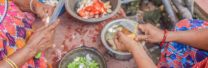 Cooking pots containing a variety of vegetables and two women cutting items