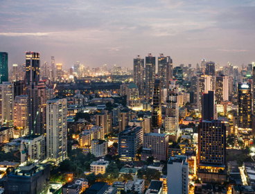 A cityscape at dusk with modern high rise buildings and lit up streets. 