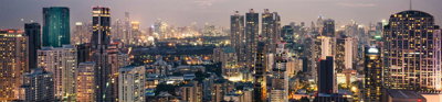 A cityscape at dusk with modern high rise buildings and lit up streets. 