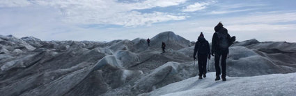 Four people walking across an undulating glacial landscape carrying equipment.