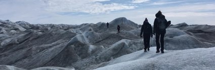 Four people walking across an undulating glacial landscape carrying equipment. 