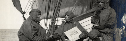 Black and white photograph of three people on a boat dressed in waterproof gear. They're smiling and eating chocolate from a box of Fry's Chocolate.