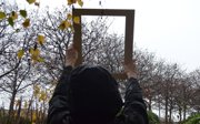 A person seen from behind holding up a wooden frame against a backdrop of barren trees.