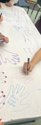 Five children draw hand prints on a large piece of white paper on which they also write words including black lives matter, polar bears and depression.