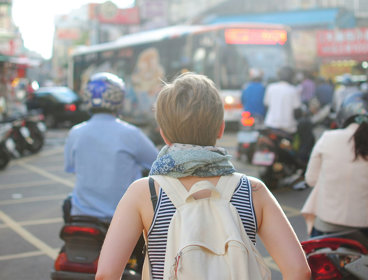 Person wearing backpack walking on road in busy city.