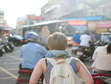 woman wearing backpack walking on road in busy city