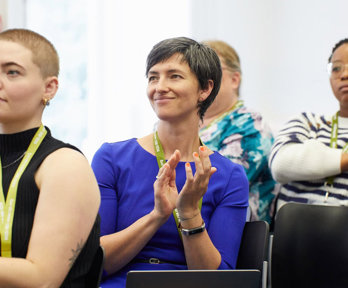 Three conference delegates listening to a presentation and apploading.