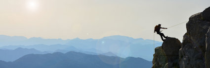 A lonely mountaineer climbing a mountain top, against a backdrop of a vast mountain range.