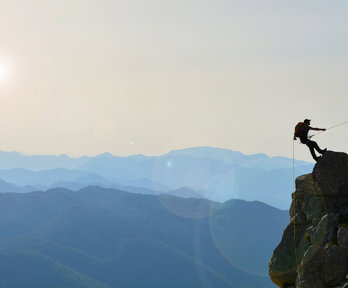 A lonely mountaineer climbing a mountain top, against a backdrop of a vast mountain range.