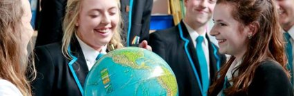 A geography ambassador showing a globe to a group of students, all of whom are smiling