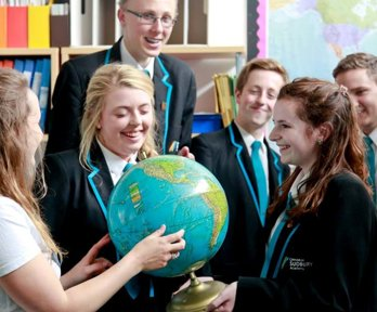 A geography ambassador showing a globe to a group of students, all of whom are smiling