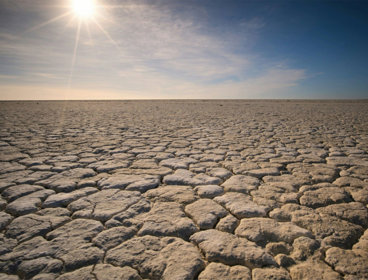 Dry, flat landscape with cracked land caused by drought. The sun is shining fiercly above the dry earth.