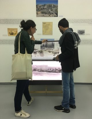 Two people stood looking at a digital image of old cars. The image is in a glass case and part of an exhibition display. 