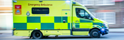 An ambulance driving at speed. The background of the picture, which is a residential street, is blurry to indicate the speed at which the vehicle is travelling.