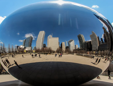 A huge silver coffee bean shaped structure in Chicago, which reflects the city skyline and blue skies