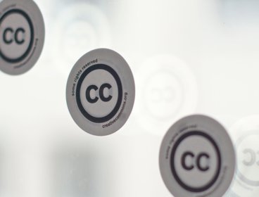 Three stickers with the creative commons logo on a window. 