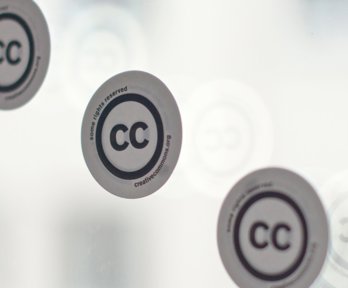 Three stickers with the creative commons logo on a window. 