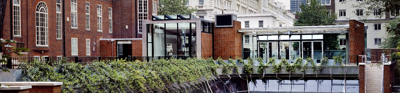 A grass covered patio bordered by a rectangular stone path. This lays surrounded by the red bricked Society building.