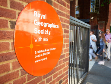 Sign on the outside of the Society's building close to the entrance, with three people walking in.