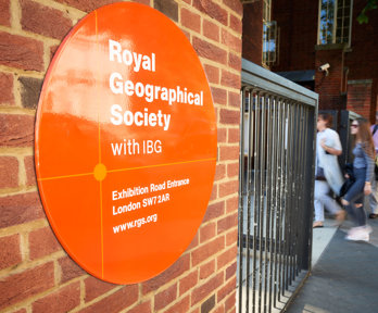 Sign on the outside of the Society's building close to the entrance, with three people walking in.