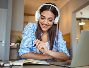 Person wearing headphones smiles while studying with a notebook and laptop.